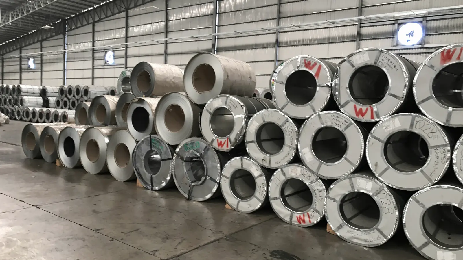Illustrative image of a warehouse aisle lined with steel coils (not Jayesh Steel stock)